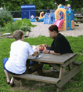 two women sit at a picnic table turned to each other and away from the playground