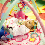 an infant lays on her back beneath dangling age-appropriate toys