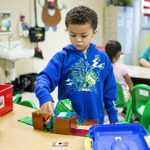 a boy stands at a low shelf assembling a toy