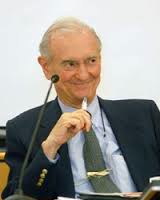 A photo of Dr. Wolf Wolfensberger sitting before a microphone with a pen in his hand.