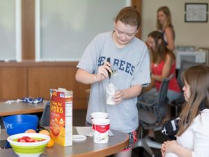 A girl in a grey tee shirt prepares a parfait.