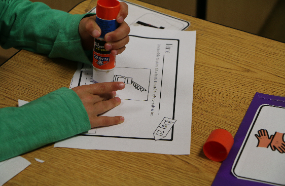 A student uses glue on paper at a desk.