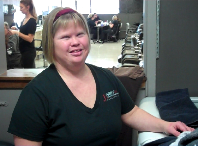 A woman stands beside a dryer in a beauty salon, folding laundry.