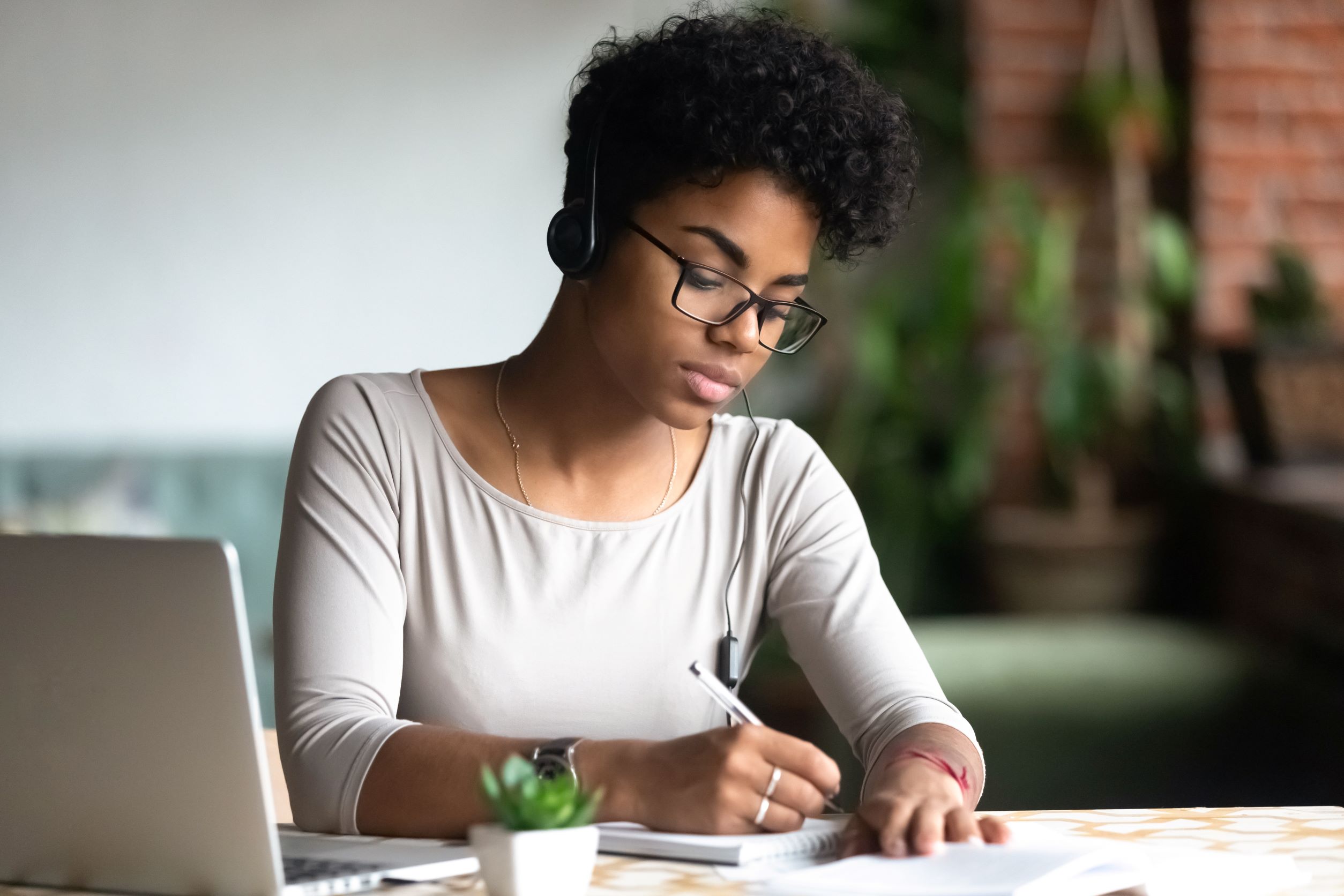 Woman wearing headphones writing in a notebook.