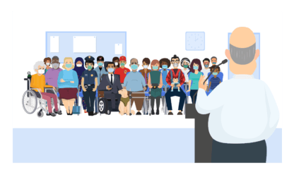 EM stands in front of a community meeting. About 20 people sit in a meeting room, wearing face masks.