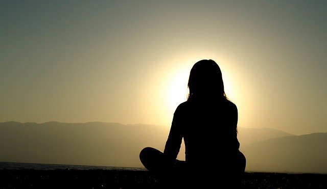 silhouette of person sitting looking at sunset
