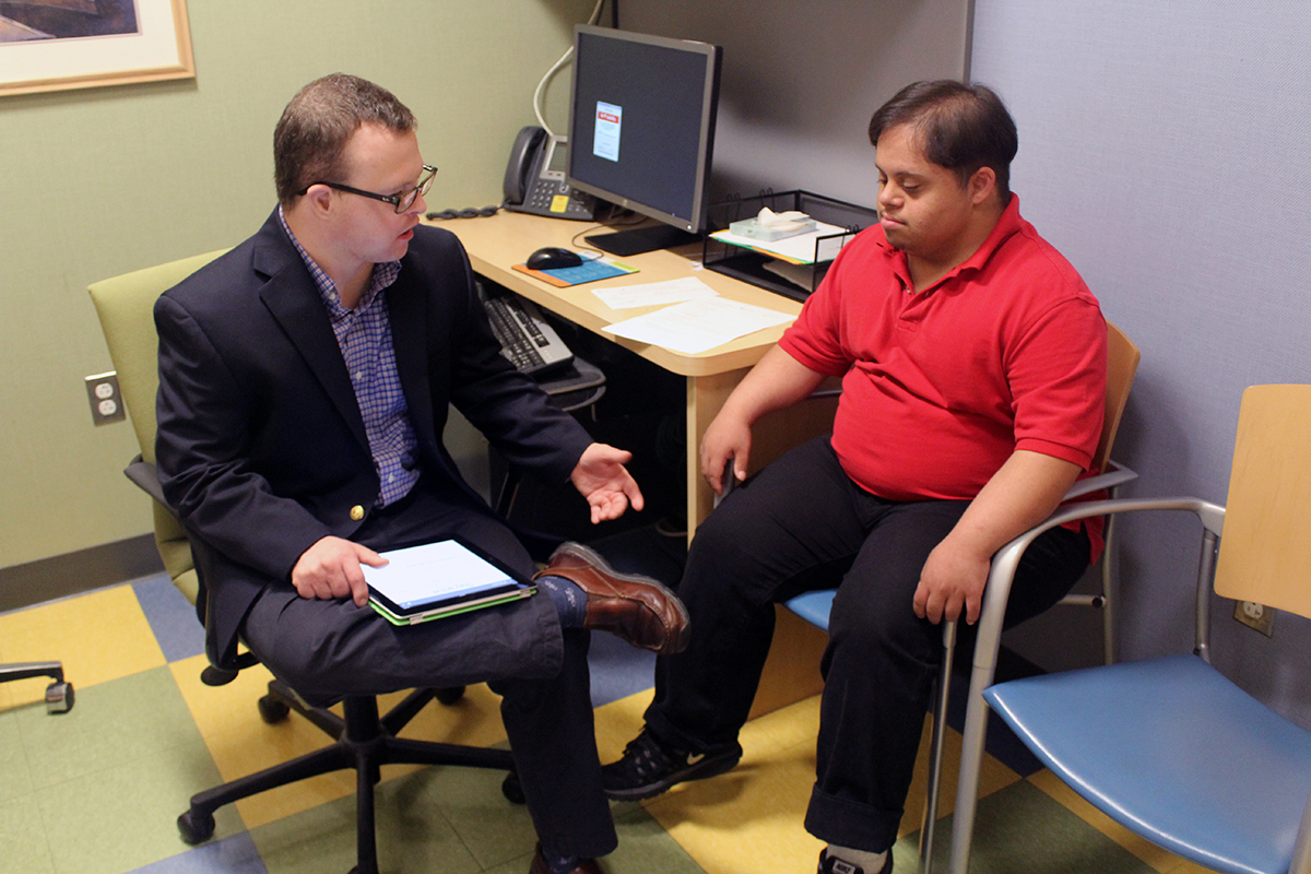 White man with Down syndrome sitting and discussing with a Latino man with Down syndrome.
