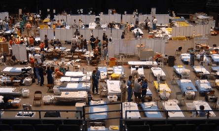 An aerial image of a crowded emergency shelter with many people, beds, and supplies