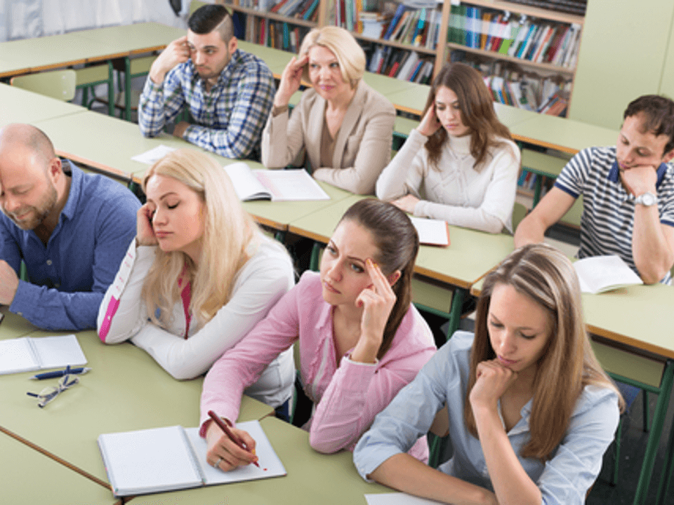 People sitting at table taking notes looking tired or bored.