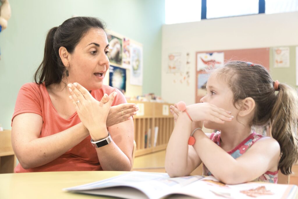 Teacher and child at a table using sign language.