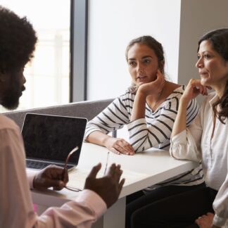 Adult at computer talking to two other adults sitting across from him.