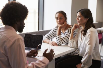 Adult at computer talking to two other adults sitting across from him.