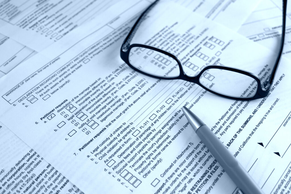A pair of black glasses and a gray pen on a stack of documents.
