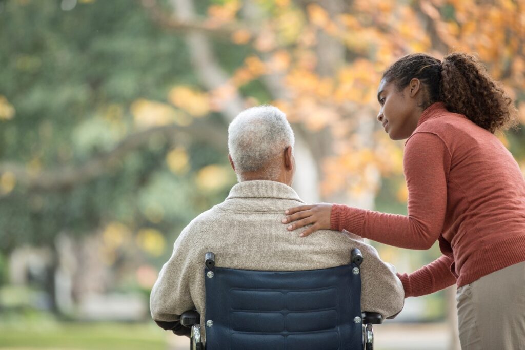 Woman with hand on the back of a man in a wheelchair.