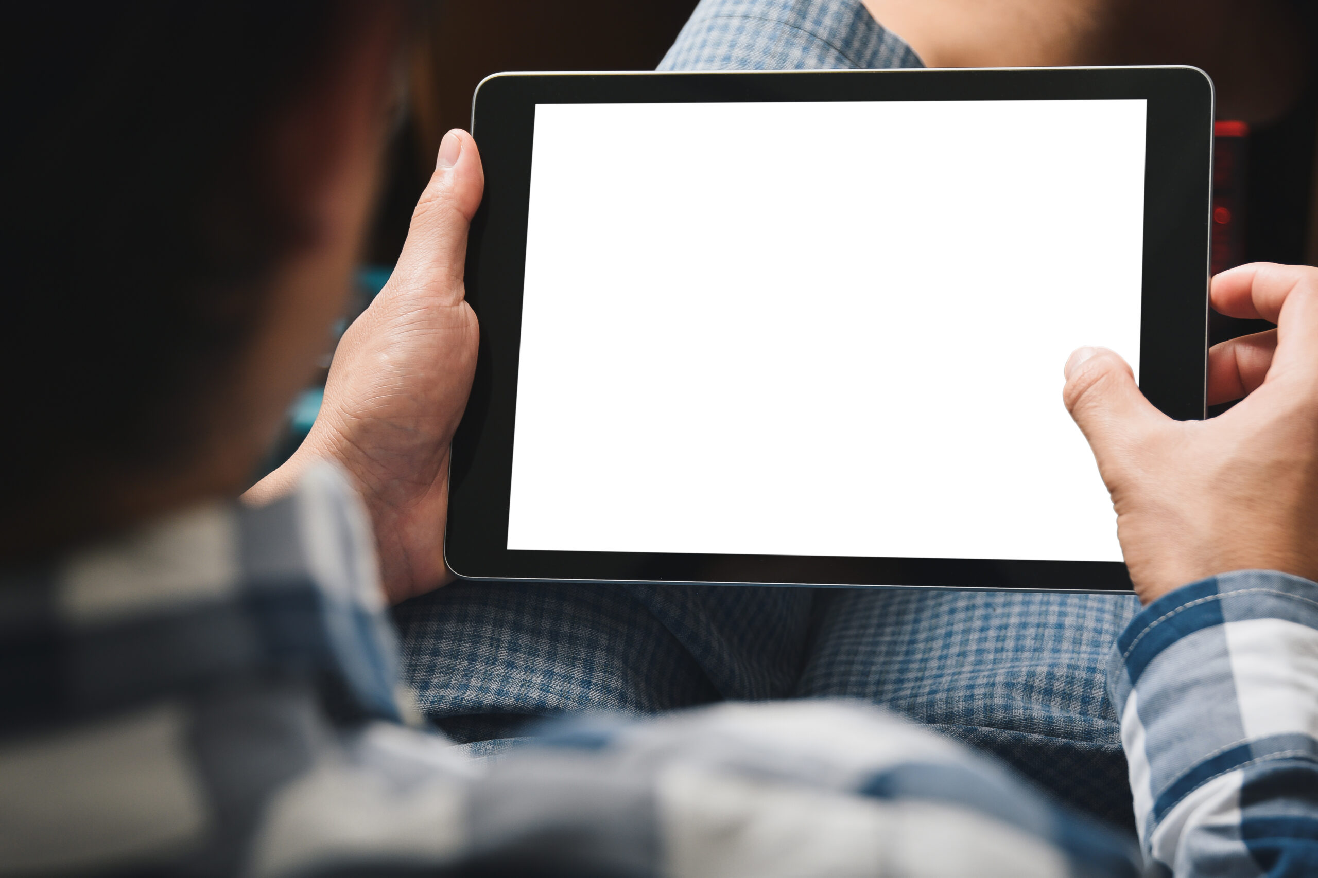 A seated person holding an iPAD wearing a checkered shirt