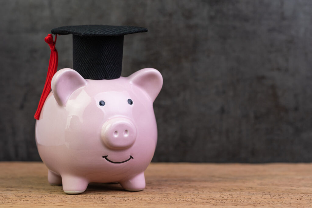 Smiling pink piggy bank wearing graduated hat on wooden table with dark black background and copy space, education fund, Scholarships, university cost and expense or saving for student loan concept.