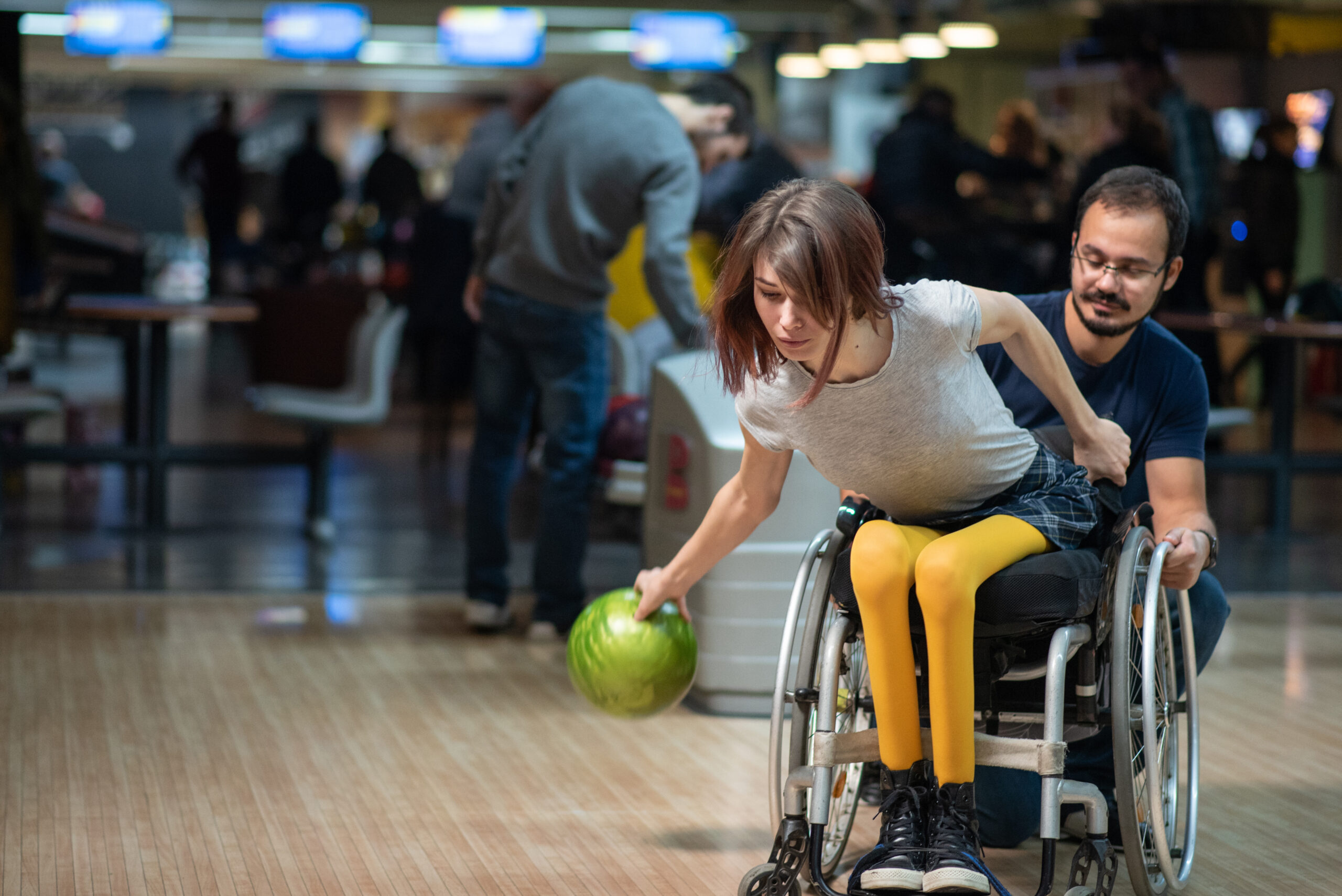 Recreation at a bowling lane, a female wheelchair users holds a green ball ready to roll