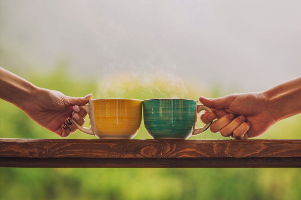 Two hands holding yellow and green tea cups on a wooden table.