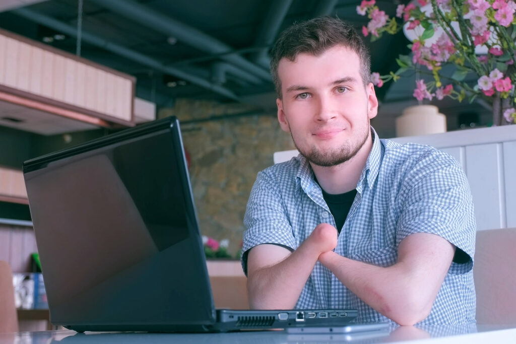 A young adult male with a blue shirt sitting in front of a computer.