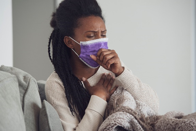 a woman wearing a purple mask coughs