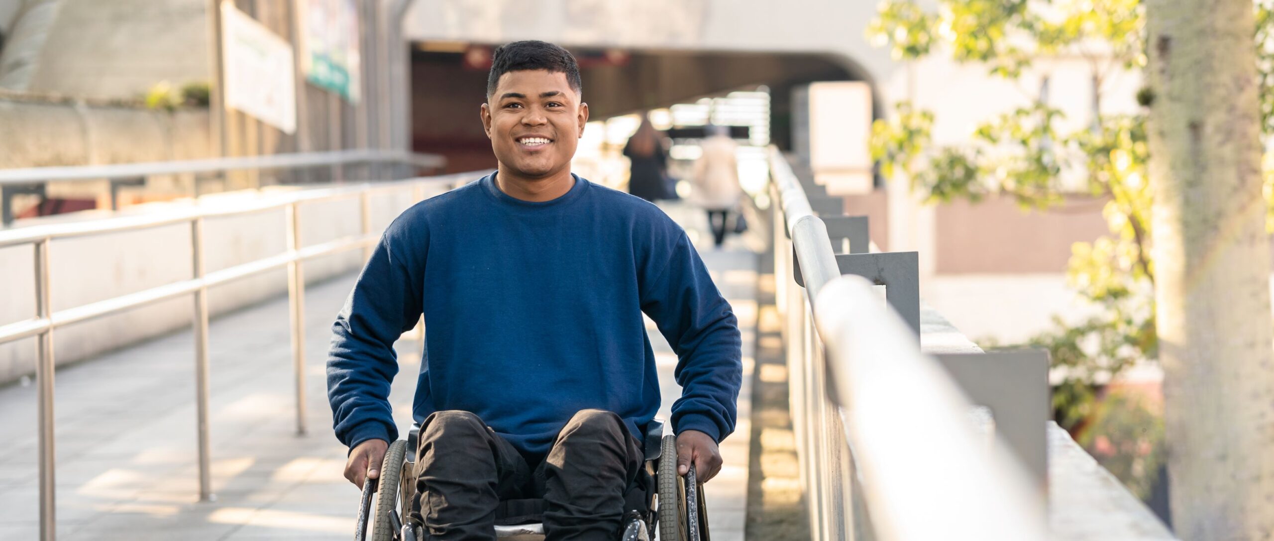 Young man sitting in a wheelchair wearing a blue shirt and black pants.