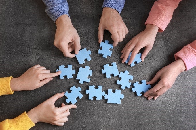 Three pairs of hands working together to put together blue puzzle pieces.