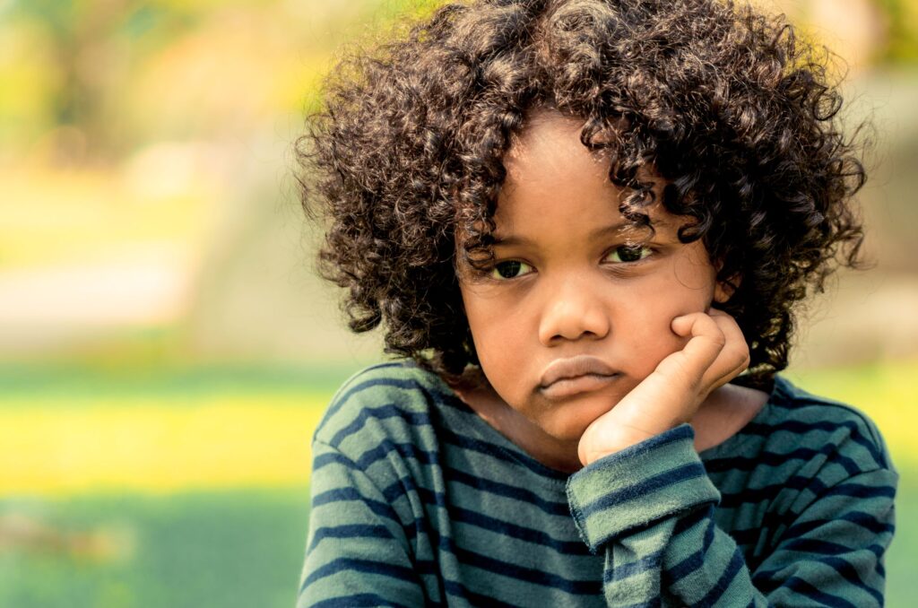 Child wearing a striped shirt with hand on chin. Appears sad.