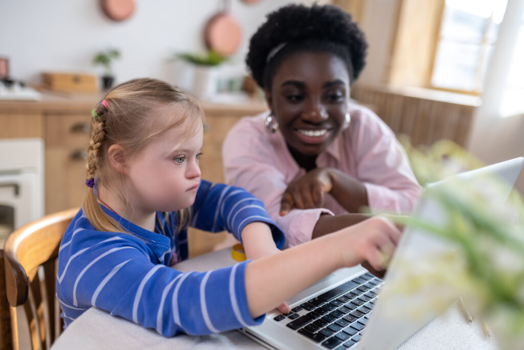 Girl on laptop with a person smiling and helping her.