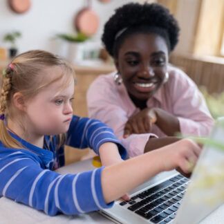 Girl on laptop with a person smiling and helping her.