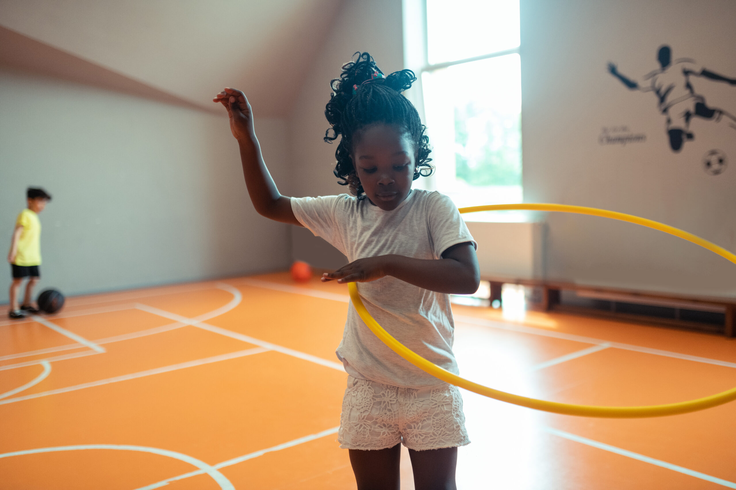 A girl using a hula hoop in an indoor gross motor area.