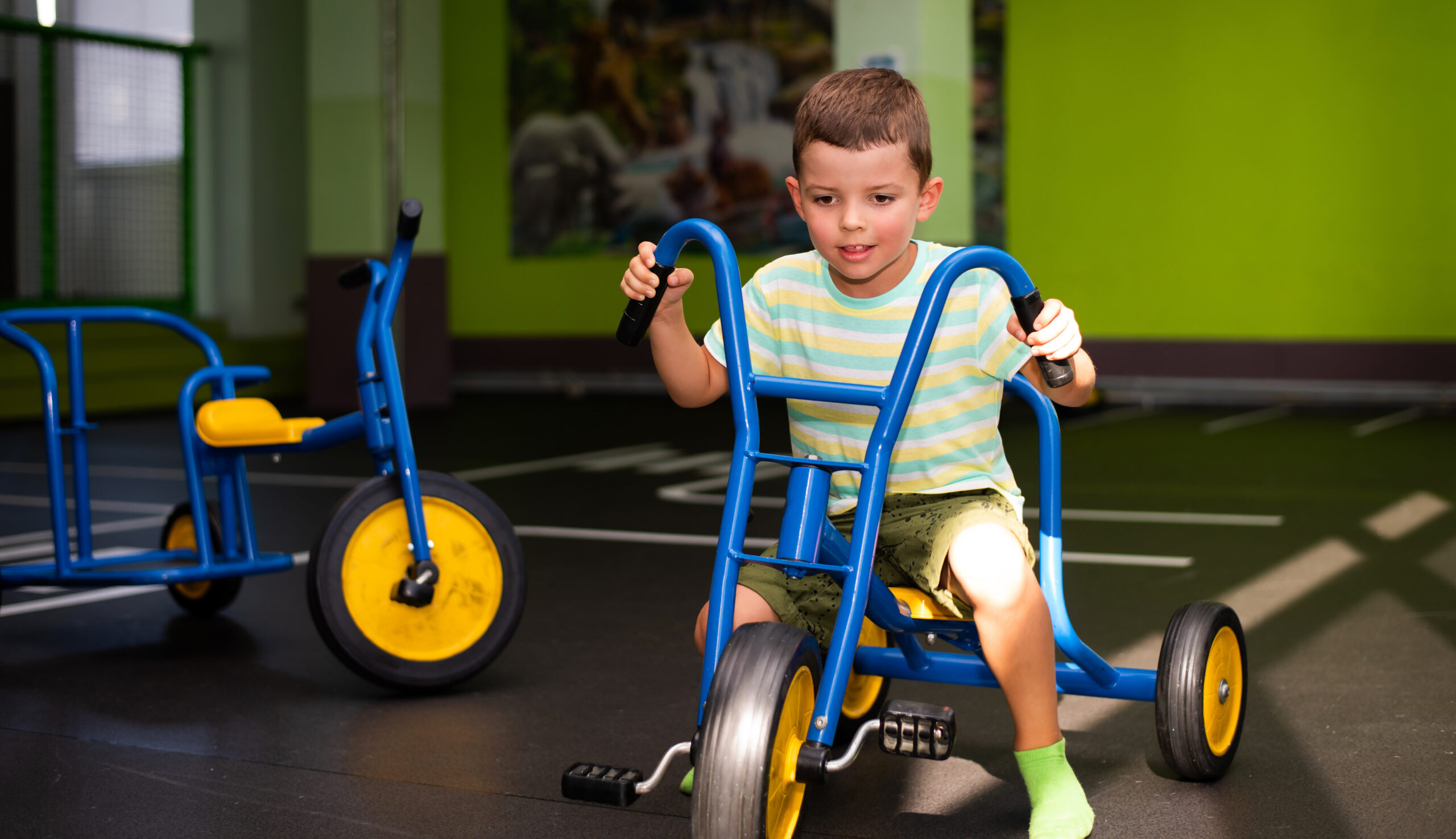 Boy on a tricycle in an indoor gross motor area.