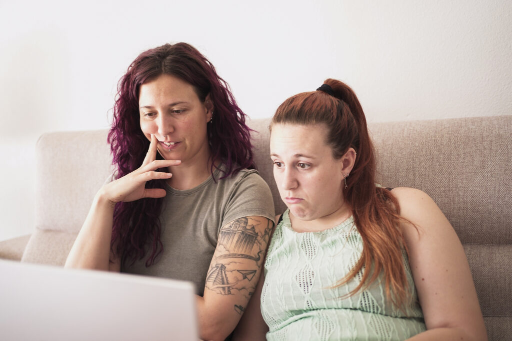 Two women sitting on a couch looking at a computer.
