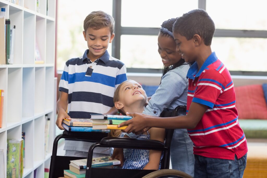 A group of students surrounding a girl in a wheelchair with books. 